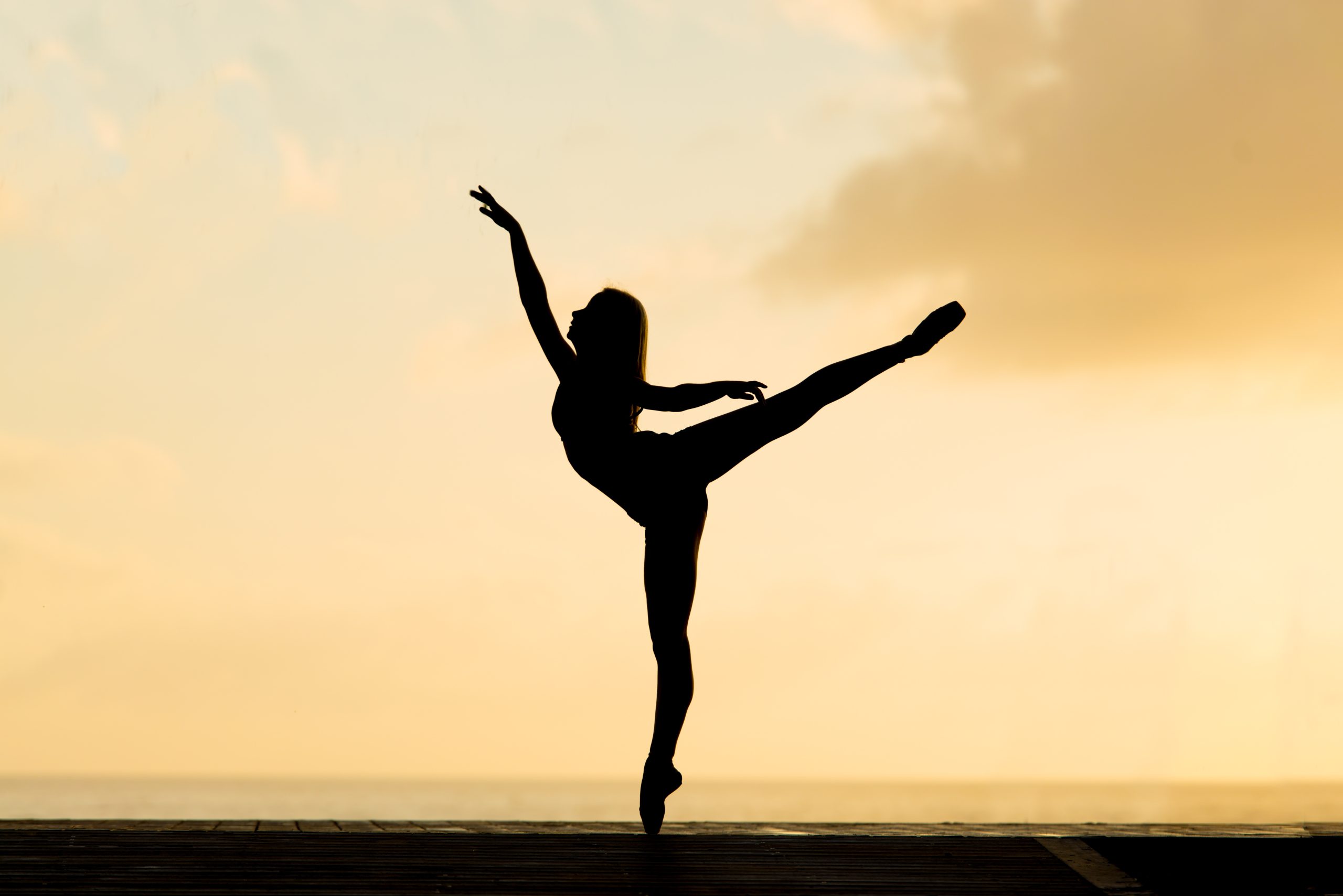 silhouette of dancer standing on toe with leg and arm extended above head