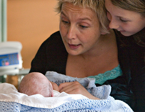 Photo of mother and daughter speaking to a newborn baby.