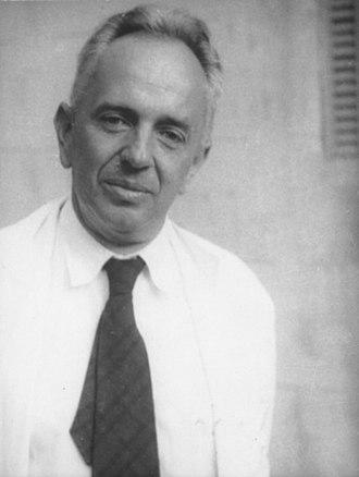 A white man with short hair dressed in a white shirt and dark tie.