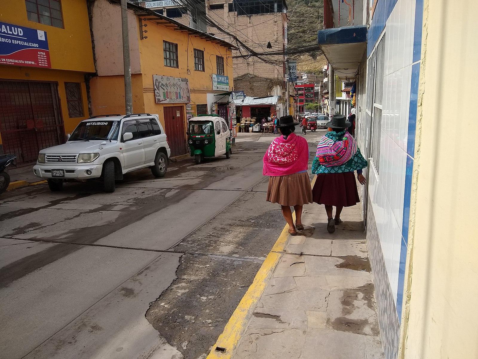 Two people walking down a street wearing brightly colored woven traditional clothing.