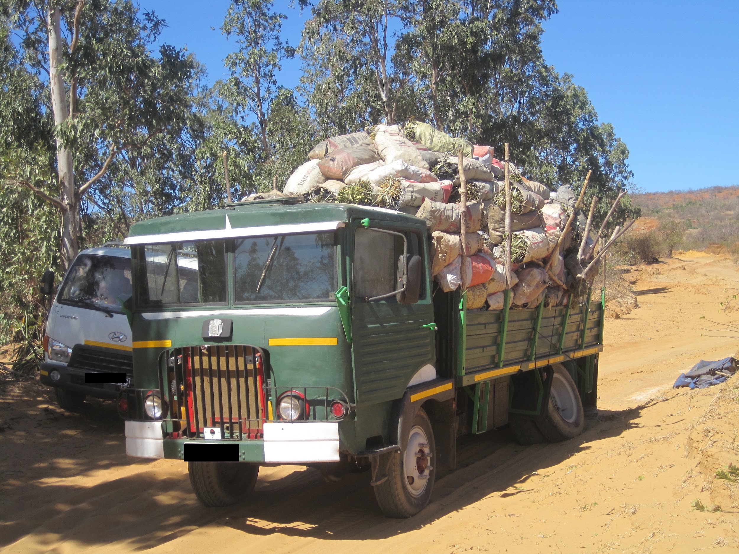 A truck on a dirt road with bags of charcoal in its bed.