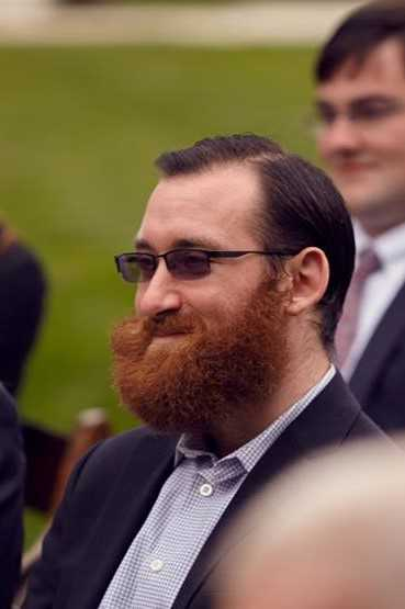 A man with glasses and a full beard smiles and looks off to the side.